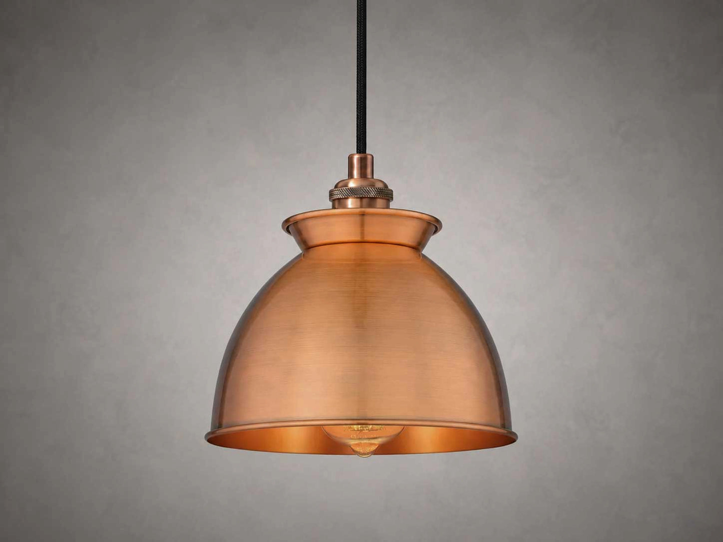 An antique copper dome pendant light with a black hanging cord, shown against a textured gray background.
