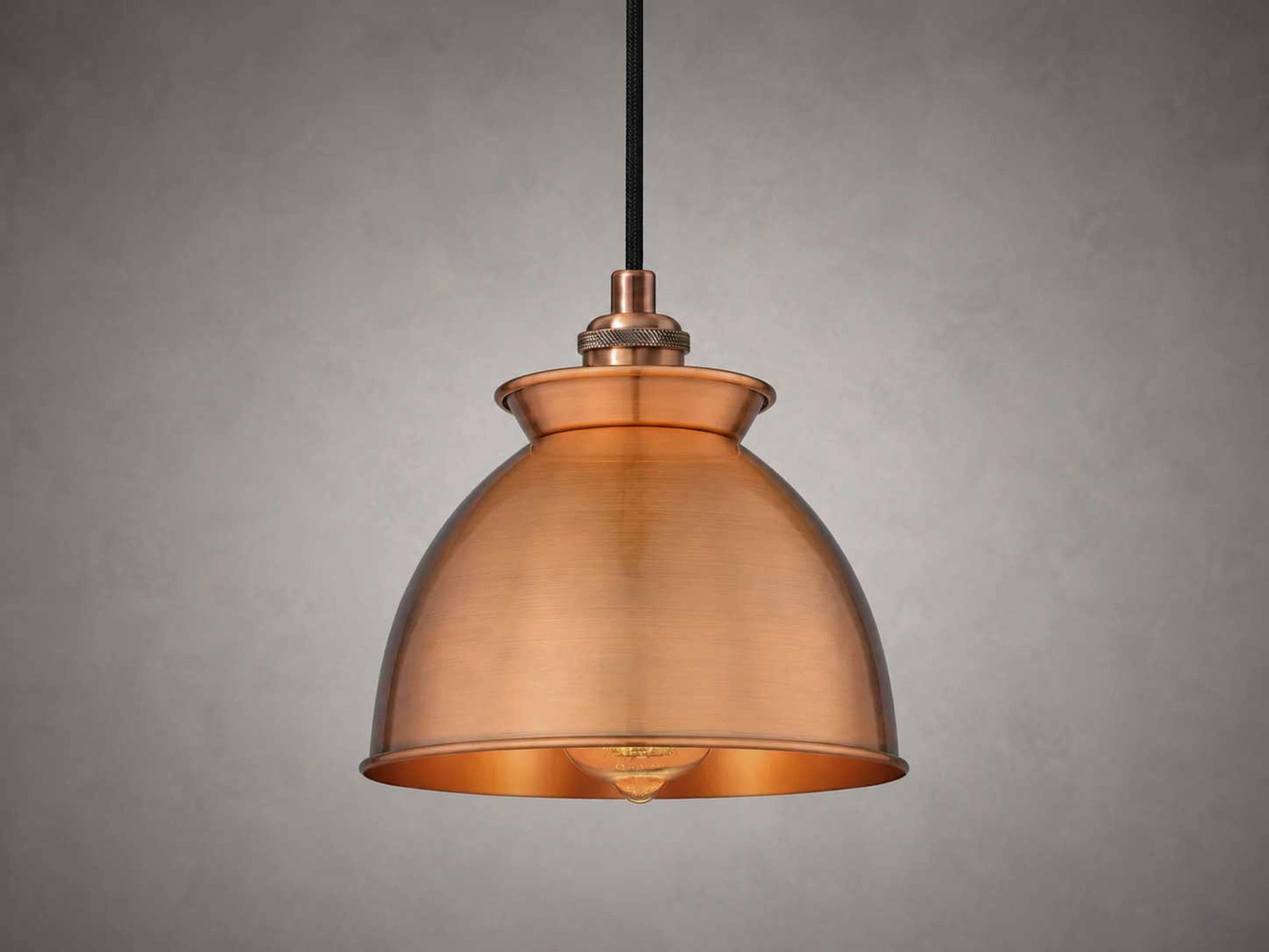 An antique copper dome pendant light with a black hanging cord, shown against a textured gray background.