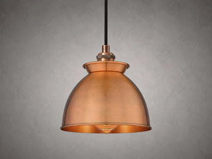 An antique copper dome pendant light with a black hanging cord, shown against a textured gray background.
